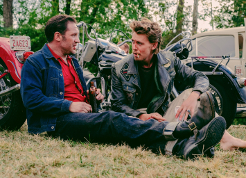 Tom Hardy as Johnny and Austin Butler as Benny sit on the grass 